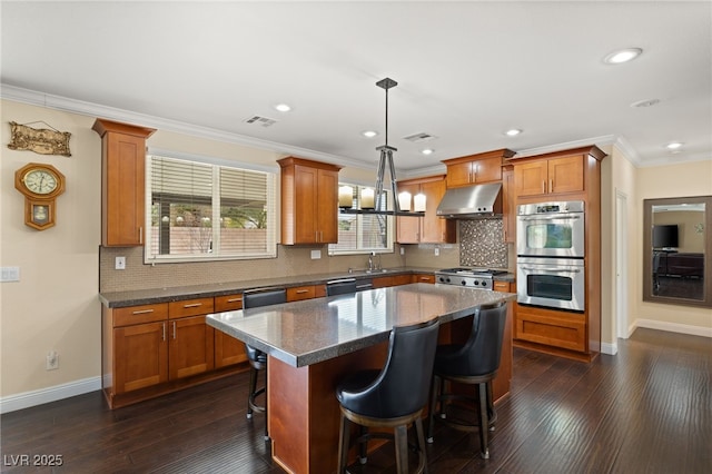 kitchen featuring double oven, hanging light fixtures, a kitchen breakfast bar, ornamental molding, and a kitchen island