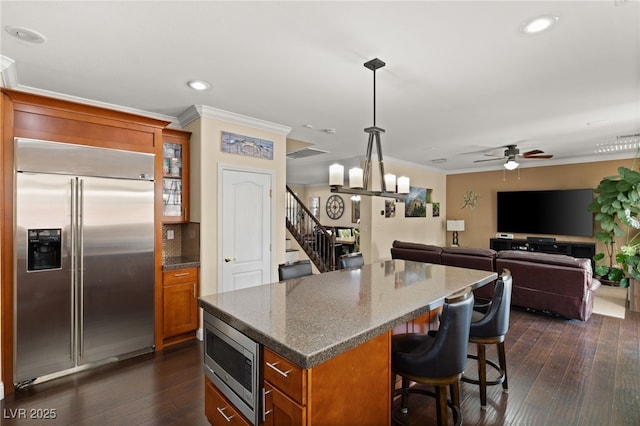 kitchen with a breakfast bar area, crown molding, built in appliances, decorative light fixtures, and dark stone countertops