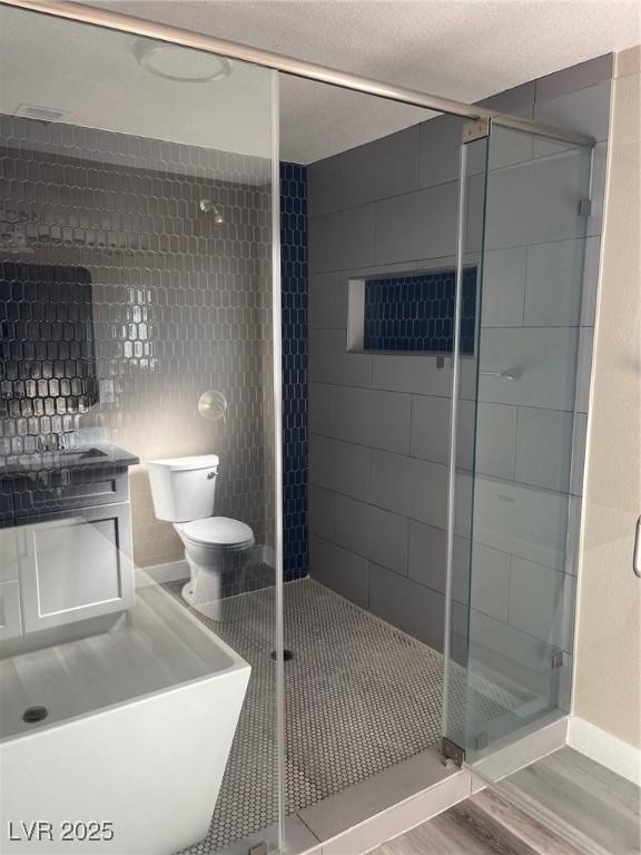 bathroom featuring toilet, hardwood / wood-style floors, a textured ceiling, and a shower with shower door