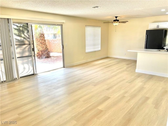 unfurnished living room with ceiling fan, sink, a textured ceiling, and light wood-type flooring