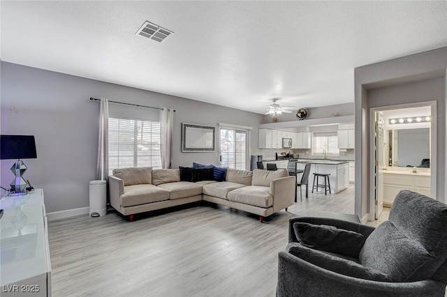 living room featuring ceiling fan, sink, light hardwood / wood-style flooring, and a textured ceiling