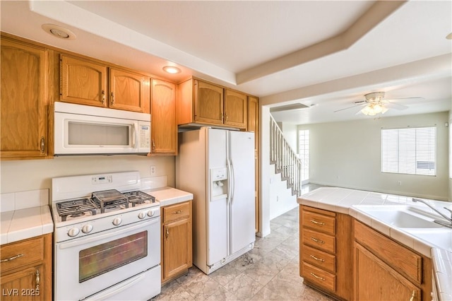 kitchen with sink, white appliances, a tray ceiling, tile counters, and ceiling fan