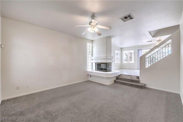 unfurnished living room featuring a multi sided fireplace, carpet flooring, and ceiling fan