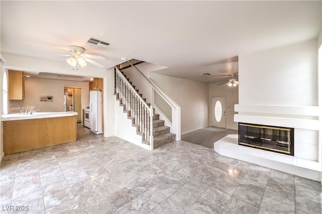 unfurnished living room featuring ceiling fan and a tile fireplace