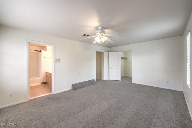 unfurnished bedroom featuring ensuite bathroom, a spacious closet, a closet, ceiling fan, and carpet