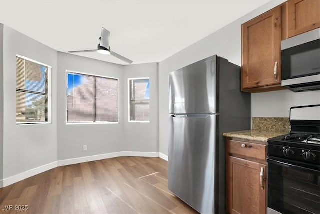 kitchen with stainless steel appliances, light wood-type flooring, light stone counters, and ceiling fan