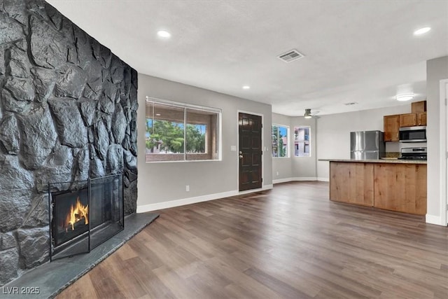 unfurnished living room with dark wood-type flooring, ceiling fan, and a stone fireplace