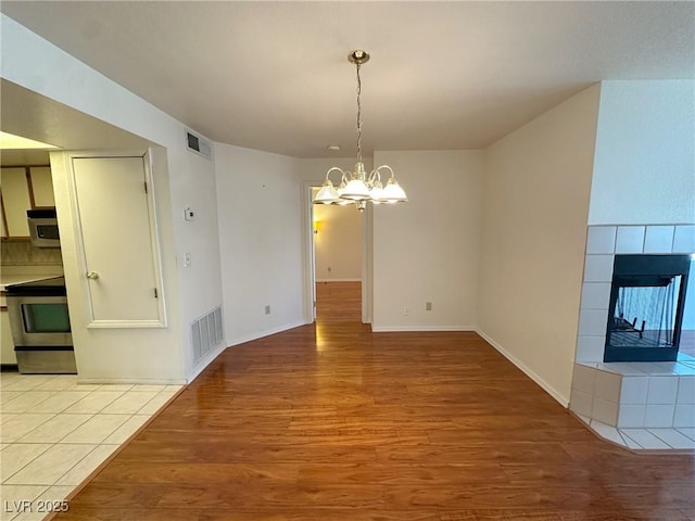 unfurnished dining area with an inviting chandelier, a tiled fireplace, and light hardwood / wood-style floors