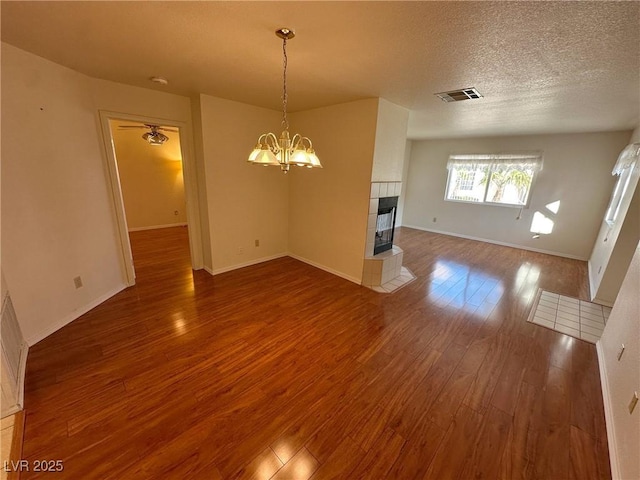 unfurnished living room with hardwood / wood-style floors, a textured ceiling, a tile fireplace, and a chandelier