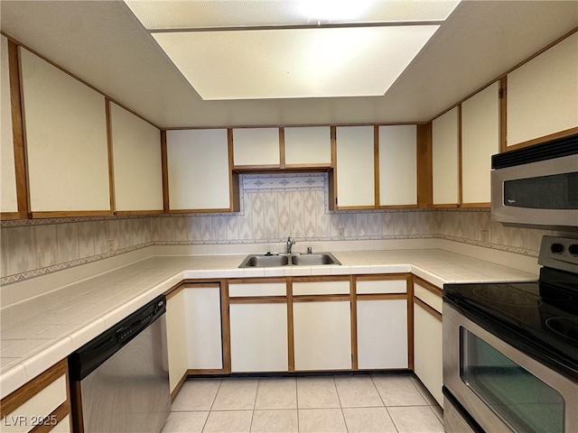 kitchen featuring sink, white cabinets, tile counters, light tile patterned floors, and stainless steel appliances