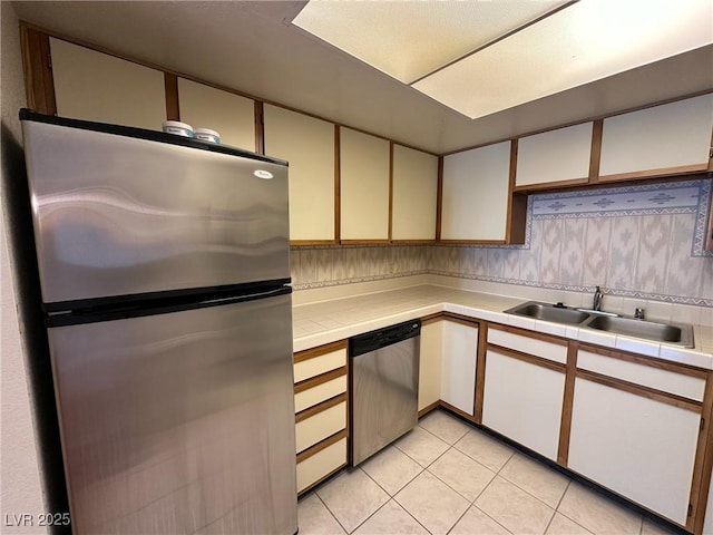 kitchen featuring sink, light tile patterned floors, tile counters, stainless steel appliances, and white cabinets