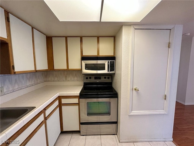 kitchen featuring light tile patterned flooring, sink, tile countertops, appliances with stainless steel finishes, and white cabinets