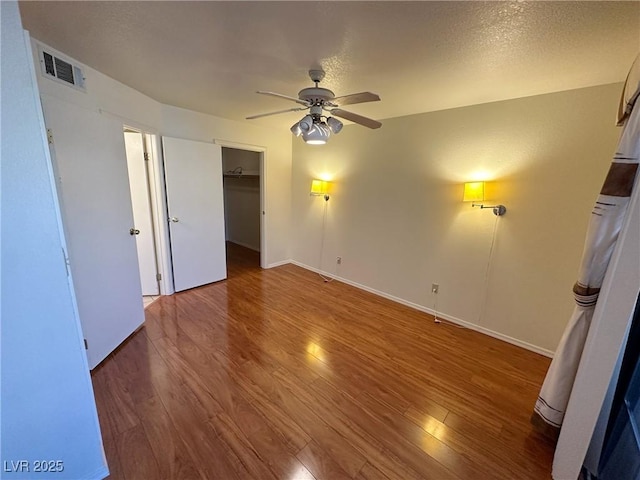 unfurnished bedroom with hardwood / wood-style flooring, a walk in closet, ceiling fan, a textured ceiling, and a closet