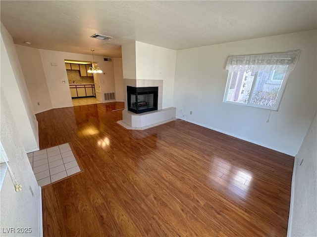 unfurnished living room featuring hardwood / wood-style flooring, a multi sided fireplace, a notable chandelier, and a textured ceiling