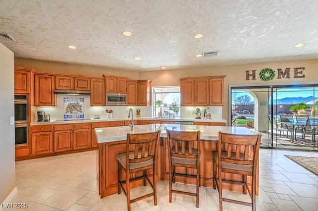 kitchen with a center island with sink, stainless steel appliances, a textured ceiling, a breakfast bar, and sink