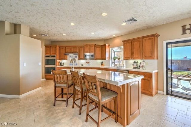 kitchen with a textured ceiling, stainless steel appliances, an island with sink, and a breakfast bar area