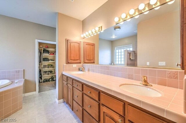 bathroom featuring a relaxing tiled tub, vanity, tile patterned flooring, and decorative backsplash