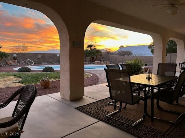 patio terrace at dusk with ceiling fan and a fenced in pool