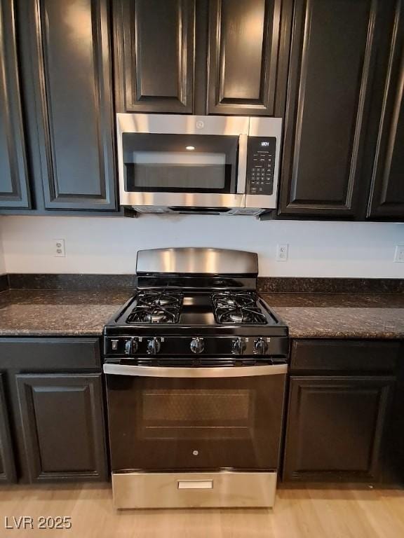 kitchen featuring black range with gas stovetop, light hardwood / wood-style floors, and dark stone counters