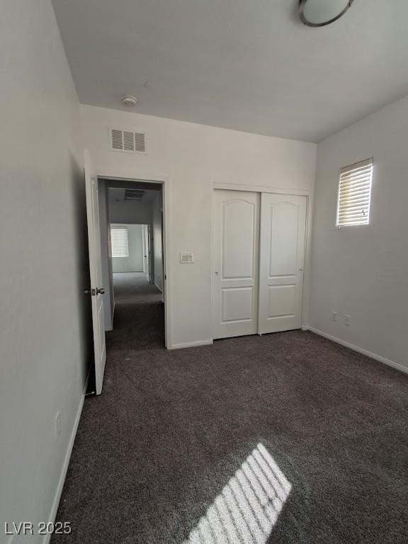 unfurnished bedroom with dark carpet and a closet