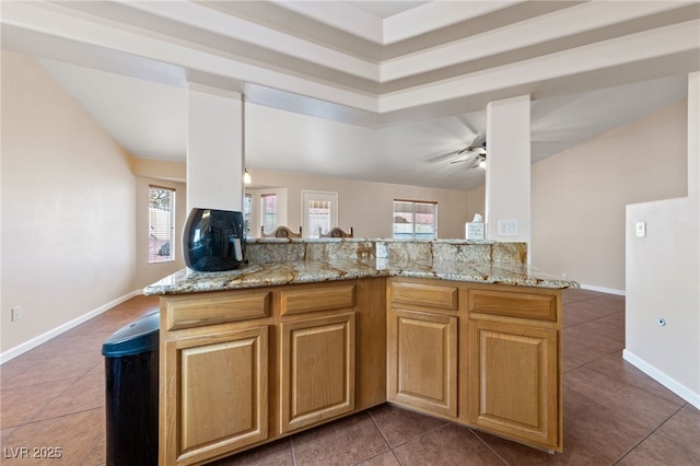 kitchen featuring dark tile patterned flooring, light stone countertops, kitchen peninsula, and ceiling fan