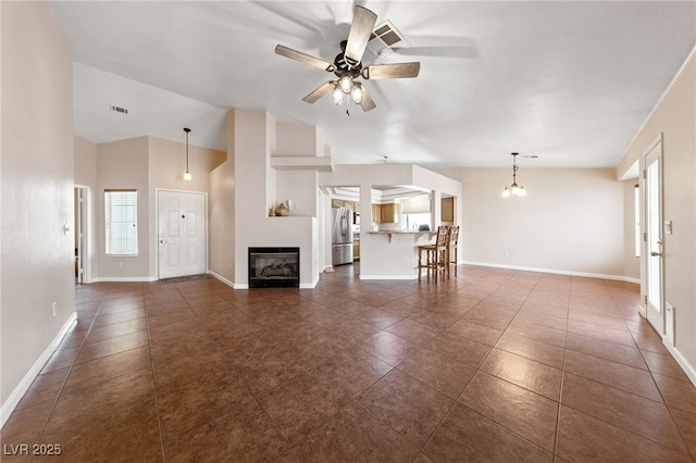 unfurnished living room featuring lofted ceiling, dark tile patterned flooring, and ceiling fan with notable chandelier