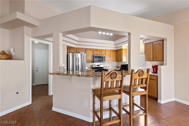 kitchen featuring a breakfast bar area, stone countertops, a tray ceiling, dark tile patterned flooring, and stainless steel appliances