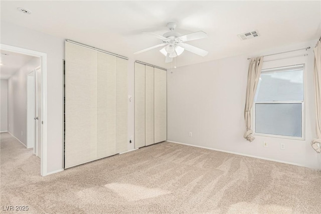 unfurnished bedroom featuring ceiling fan, light colored carpet, and two closets