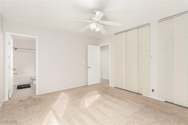 unfurnished bedroom featuring multiple closets, ensuite bathroom, light colored carpet, and ceiling fan