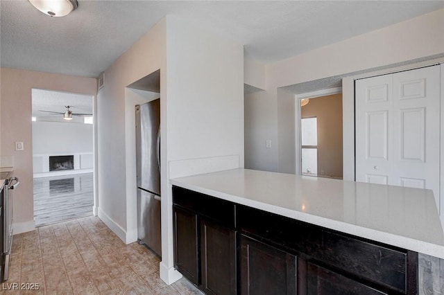 kitchen with stainless steel fridge, ceiling fan, dark brown cabinets, a textured ceiling, and built in shelves