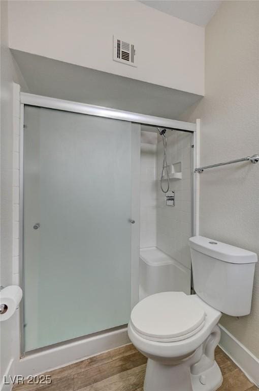 bathroom featuring hardwood / wood-style flooring, a shower with shower door, and toilet