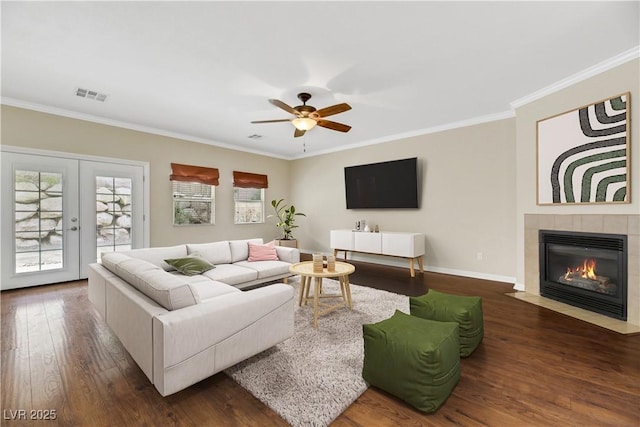 living room with french doors, ornamental molding, dark hardwood / wood-style floors, a tile fireplace, and ceiling fan