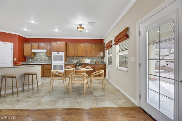 kitchen with crown molding, white double oven, tasteful backsplash, and light hardwood / wood-style flooring