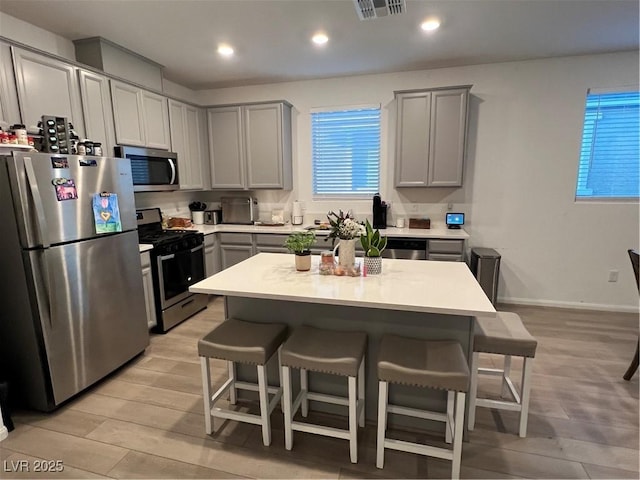 kitchen with stainless steel appliances, a breakfast bar, a kitchen island, and gray cabinetry