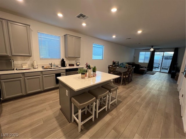 kitchen featuring a kitchen bar, a center island, light wood-type flooring, gray cabinets, and dishwasher