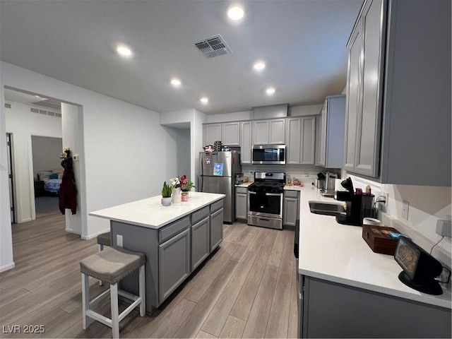 kitchen featuring stainless steel appliances, a kitchen island, gray cabinetry, and light hardwood / wood-style flooring