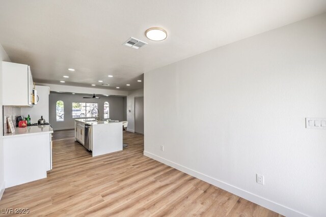 kitchen featuring ceiling fan, a kitchen island with sink, light hardwood / wood-style floors, white cabinets, and stainless steel dishwasher