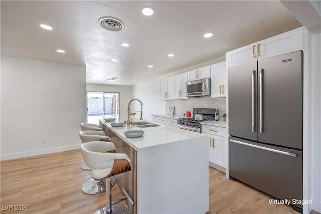 kitchen featuring appliances with stainless steel finishes, sink, white cabinets, a center island with sink, and light hardwood / wood-style flooring