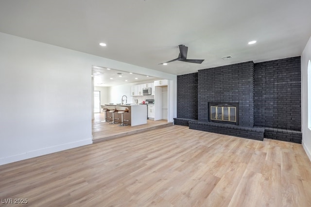 unfurnished living room featuring visible vents, light wood-style floors, a brick fireplace, and ceiling fan