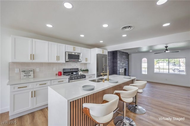 kitchen with visible vents, decorative backsplash, appliances with stainless steel finishes, white cabinetry, and a kitchen island with sink