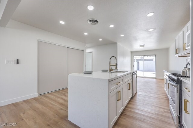 kitchen with white cabinetry, sink, stainless steel appliances, a center island with sink, and light hardwood / wood-style flooring