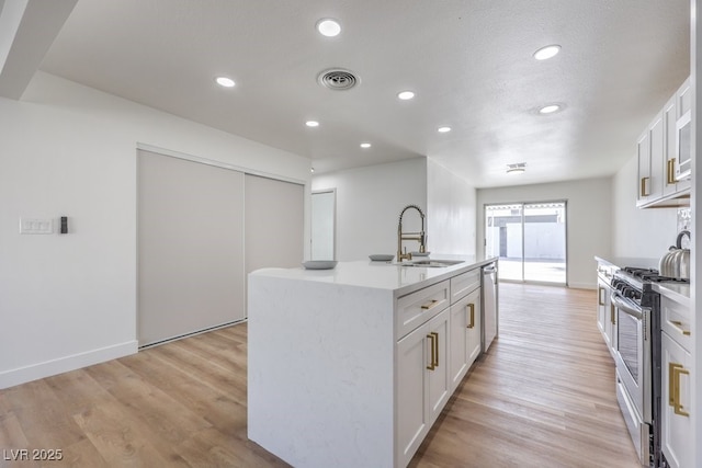 kitchen with light wood finished floors, visible vents, light countertops, appliances with stainless steel finishes, and a sink