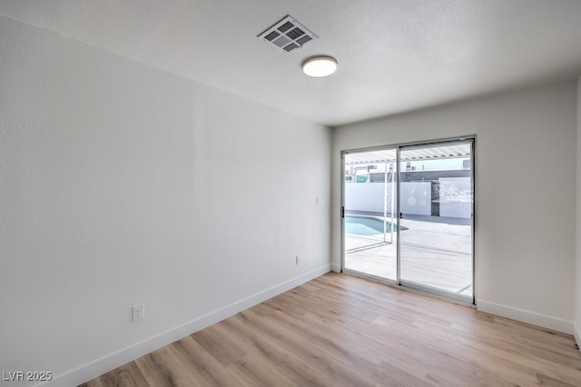 empty room featuring a textured ceiling, baseboards, visible vents, and light wood-type flooring