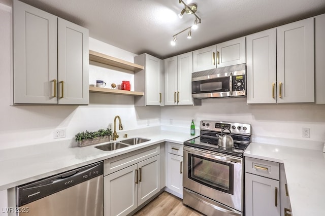 kitchen featuring sink, stainless steel appliances, light hardwood / wood-style floors, light stone countertops, and a textured ceiling