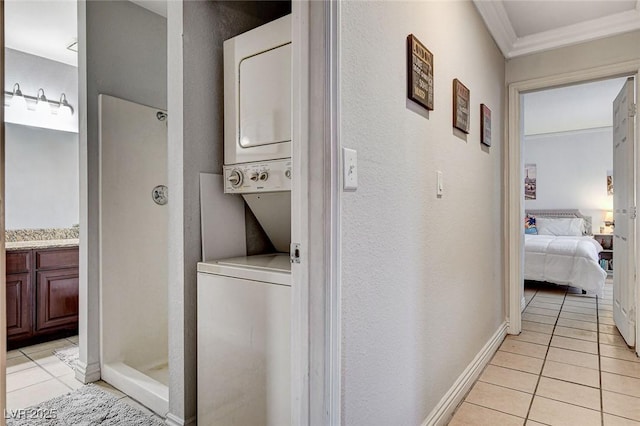 laundry room featuring light tile patterned floors, crown molding, and stacked washing maching and dryer