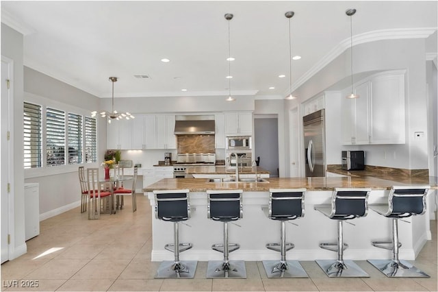 kitchen with white cabinetry, a breakfast bar, wall chimney range hood, and built in appliances