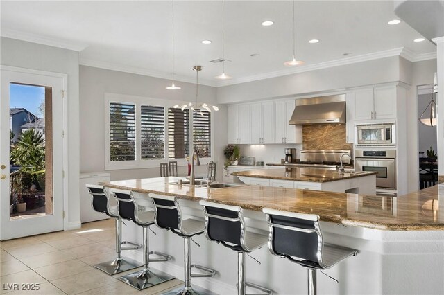 kitchen featuring pendant lighting, wall chimney range hood, appliances with stainless steel finishes, white cabinetry, and a spacious island