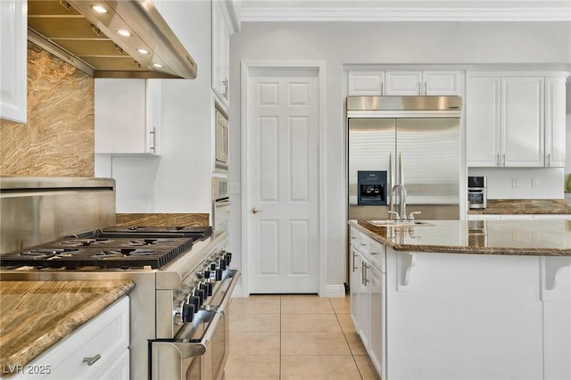 kitchen featuring sink, white cabinetry, built in appliances, ventilation hood, and dark stone counters