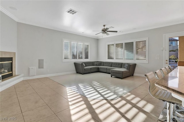 tiled living room featuring a tiled fireplace, ornamental molding, and ceiling fan