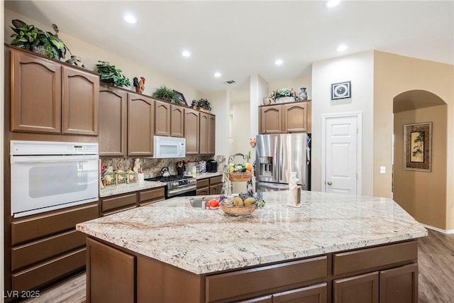 kitchen with a kitchen island with sink, backsplash, stainless steel appliances, and light wood-type flooring